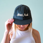 A dark greenish blue flat brim hat with white embroidered text that reads, 'North Park'.