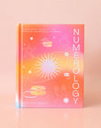 On a peachy background is a hot pink and orange book with a white title running vertically down the right side that reads, "Numerology", "A Beginner's Guide To The Spiritual Meaning of Numbers".