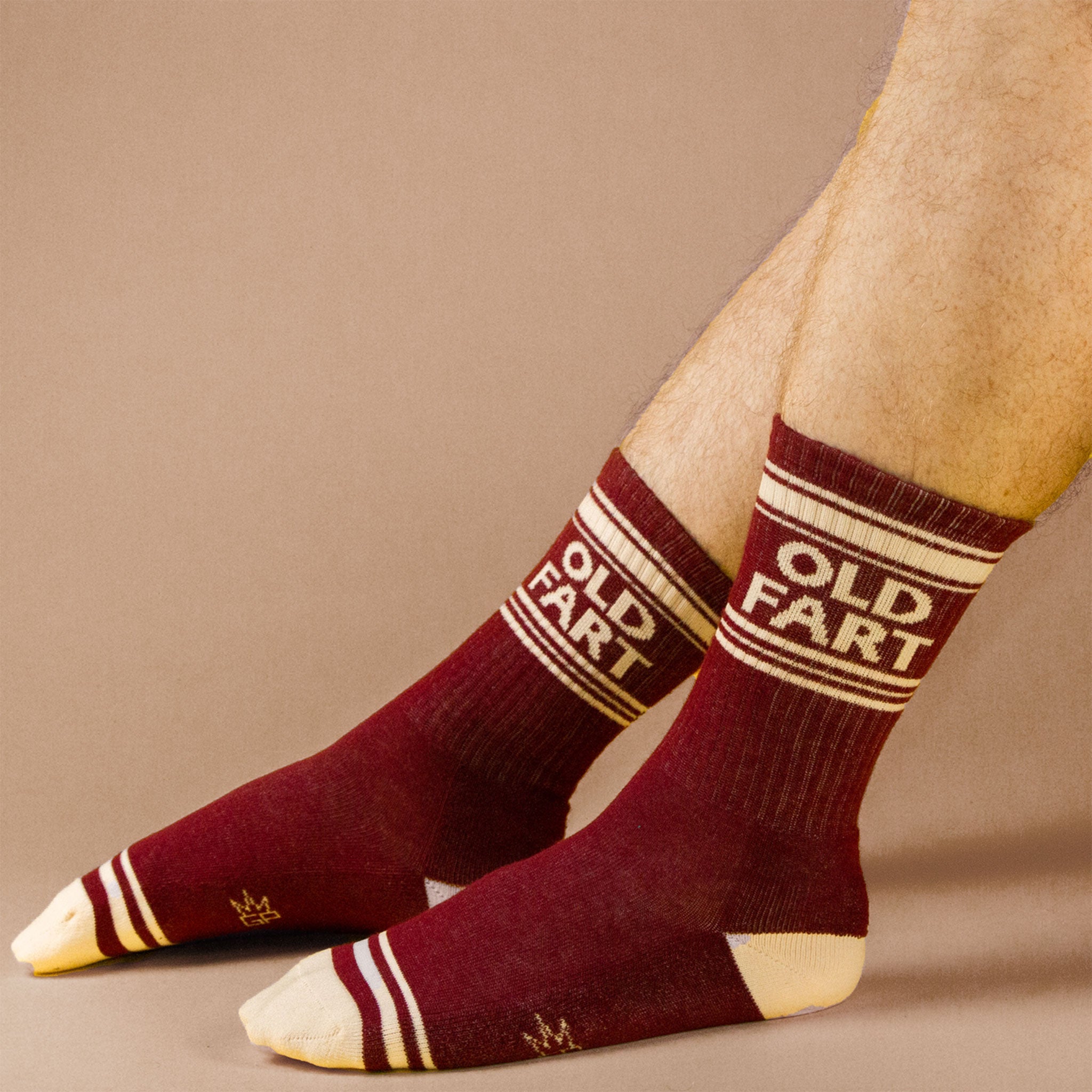 On a neutral is a model wearing a pair of dark red socks with ivory details and text at the top that reads, &quot;Old Fart&quot;.