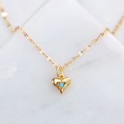 A gold chain necklace with a small gold heart shaped pendant with a blue opal in the center.