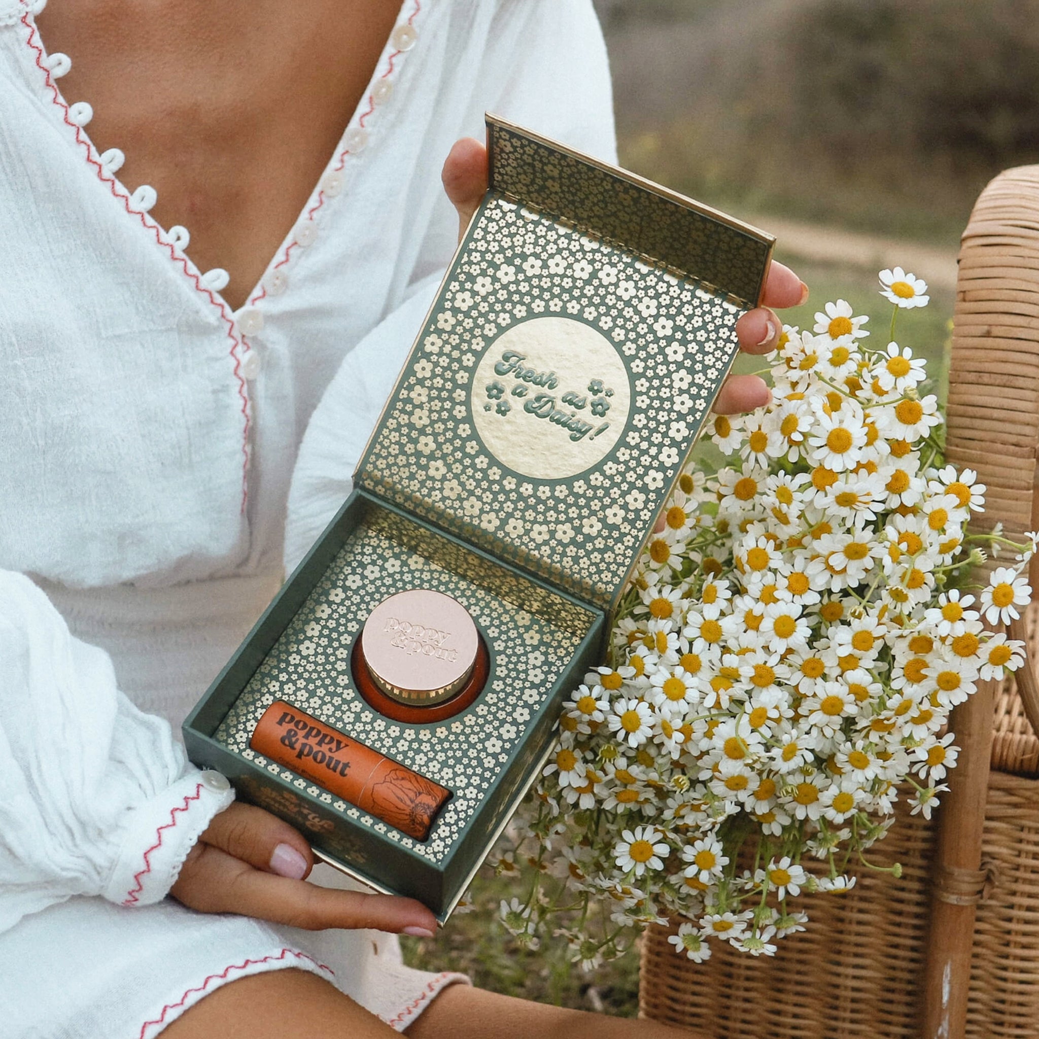 A lip duo of an orange jar of lip scrub and a tube of lip balm in the interior of the box that features a gold and green floral design. 