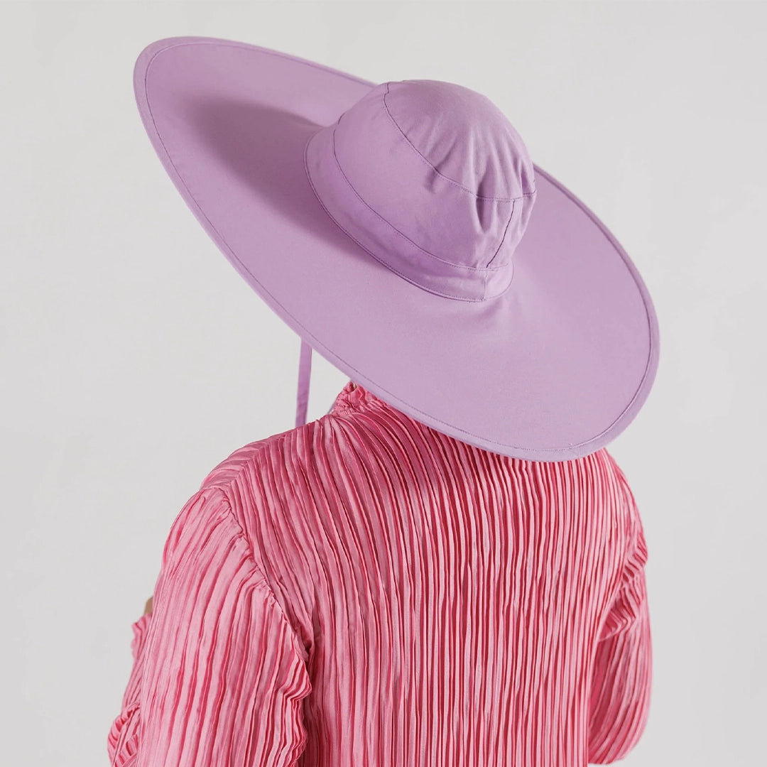 On a white background is a purple nylon sun hat that folds down for easy on the go traveling. It has a wide brim and a neck tie.