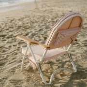 A pink and white folding beach chair with pockets, wood detailing and straps for carrying.