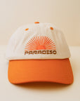 An orange and cream colored baseball cap with an embroidered sun ray design and brown text that reads, 'Paradiso'.