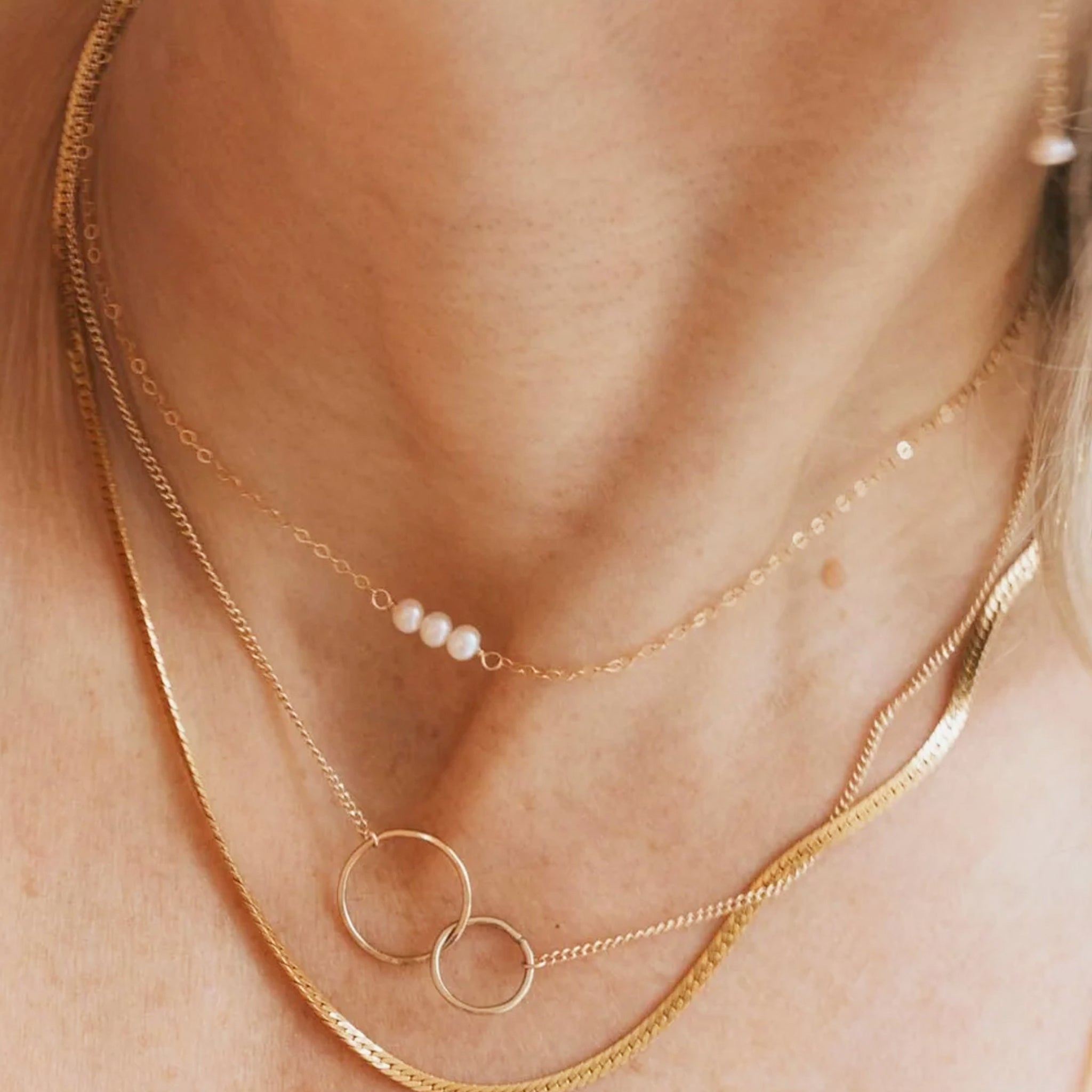A gold chain necklace with three small pearl connected in the center. 