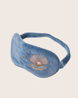 A blue velvet eye mask with an embroidered shell and pearl graphic.