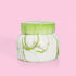 On a pink background is a green and white marble jar candle with a lid. 