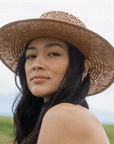 A light brown woven sun hat with details on the crown of the hat and a strap around the base.