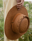 A light brown woven sun hat with details on the crown of the hat and a strap around the base.