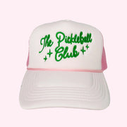 A light pink trucker hat with green embroidered text across the front that reads, "The Pickleball Club".