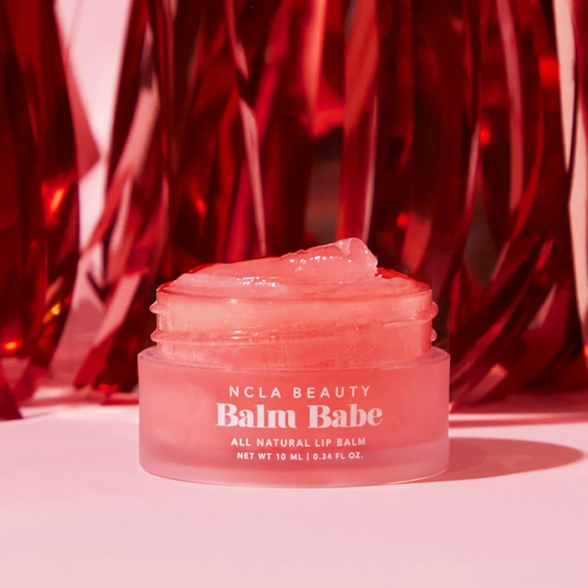 A small jar of pink lip balm on a red tinsel background. 