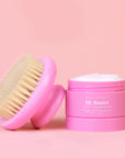 A body butter next to a pink dry brush.