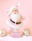 On a pink background is a Santa figurine with a pink flocked suit and white furry details.