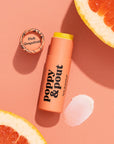 In front of white background is a round peach tube. On the right side is a black drawing of a flower. On the right side is black text that reads ‘poppy & pout, pink grapefruit lip balm.'