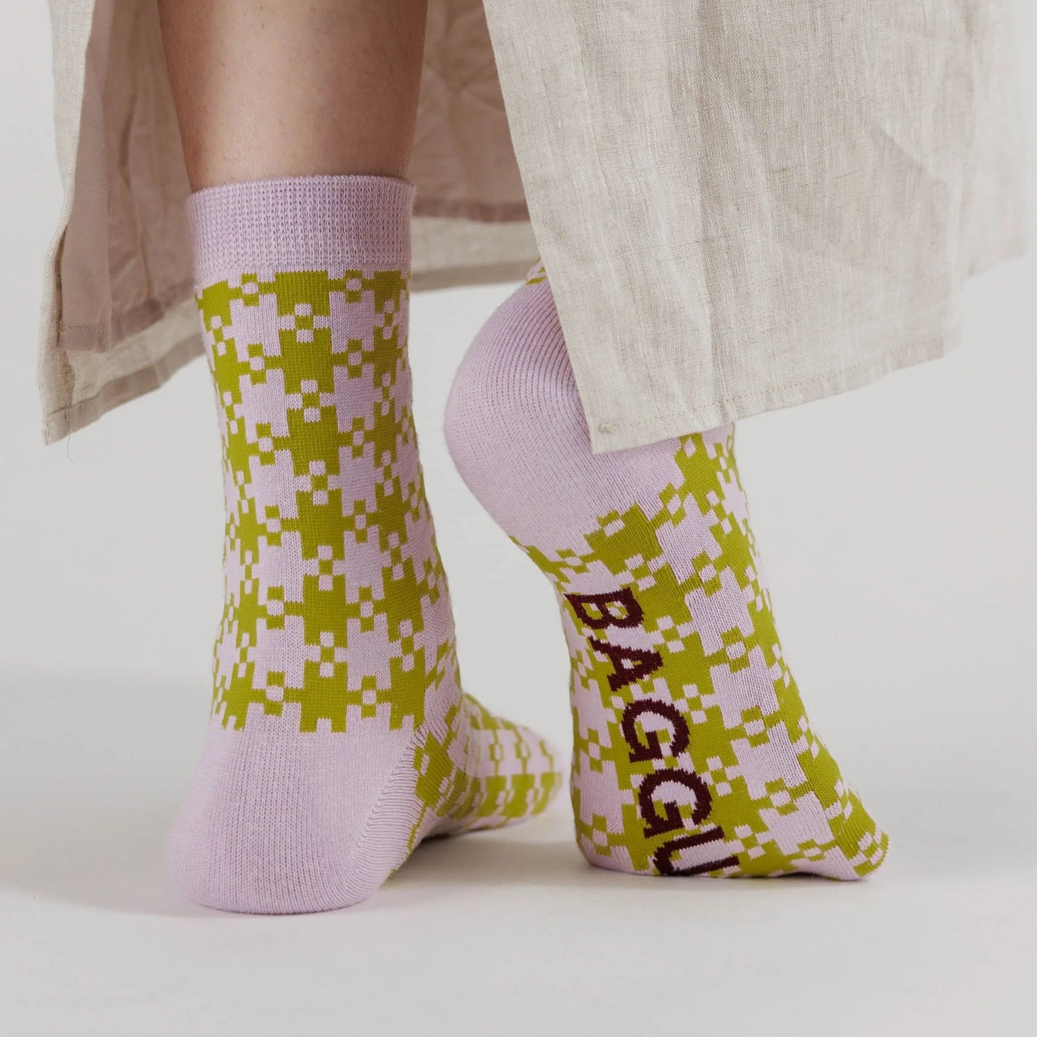On a white background is a pair of pink and green gingham printed socks.