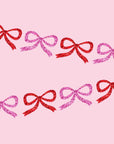A pink and red glitter bow garland made out of paper cut outs.