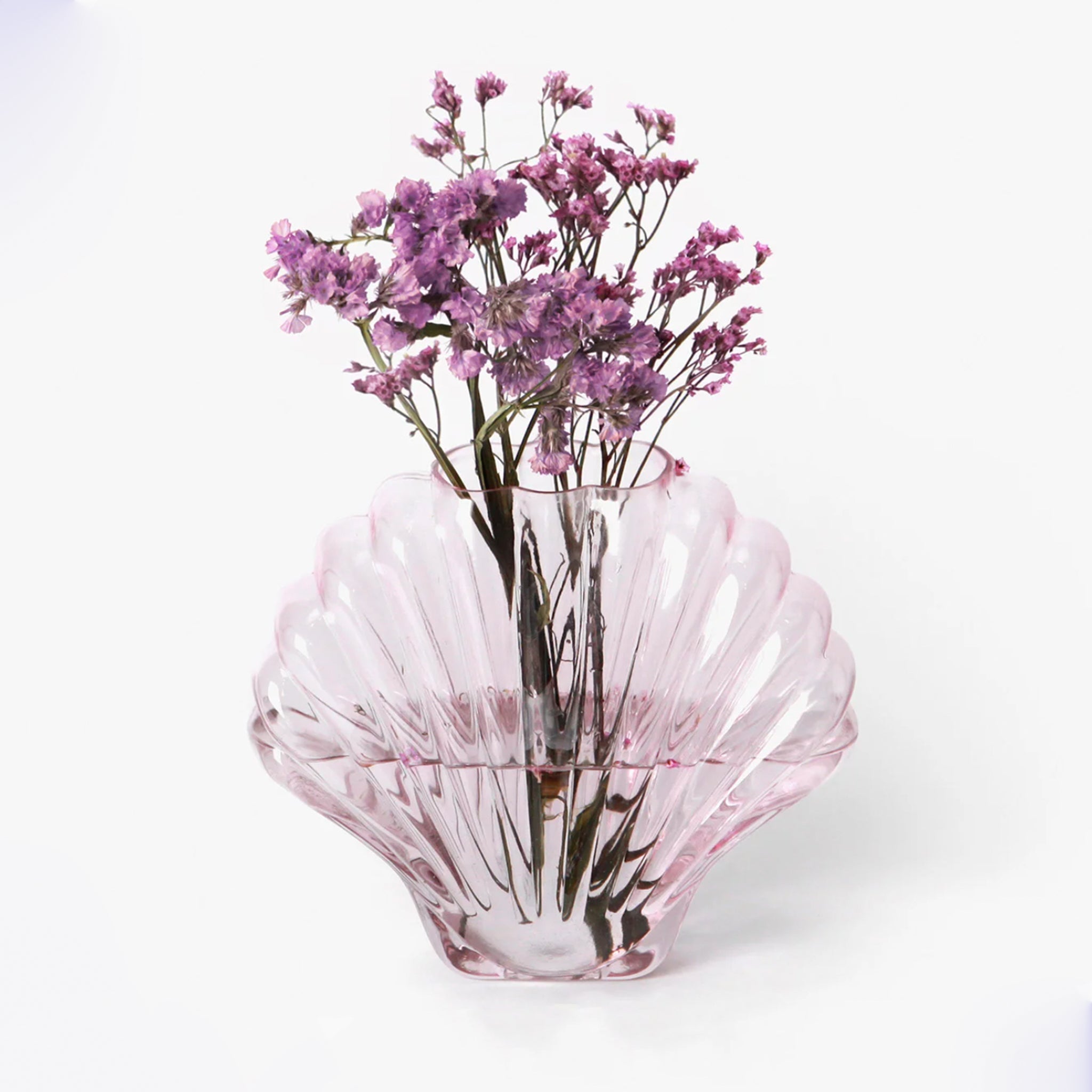 On a white background is a light pink glass, shell shaped vase.