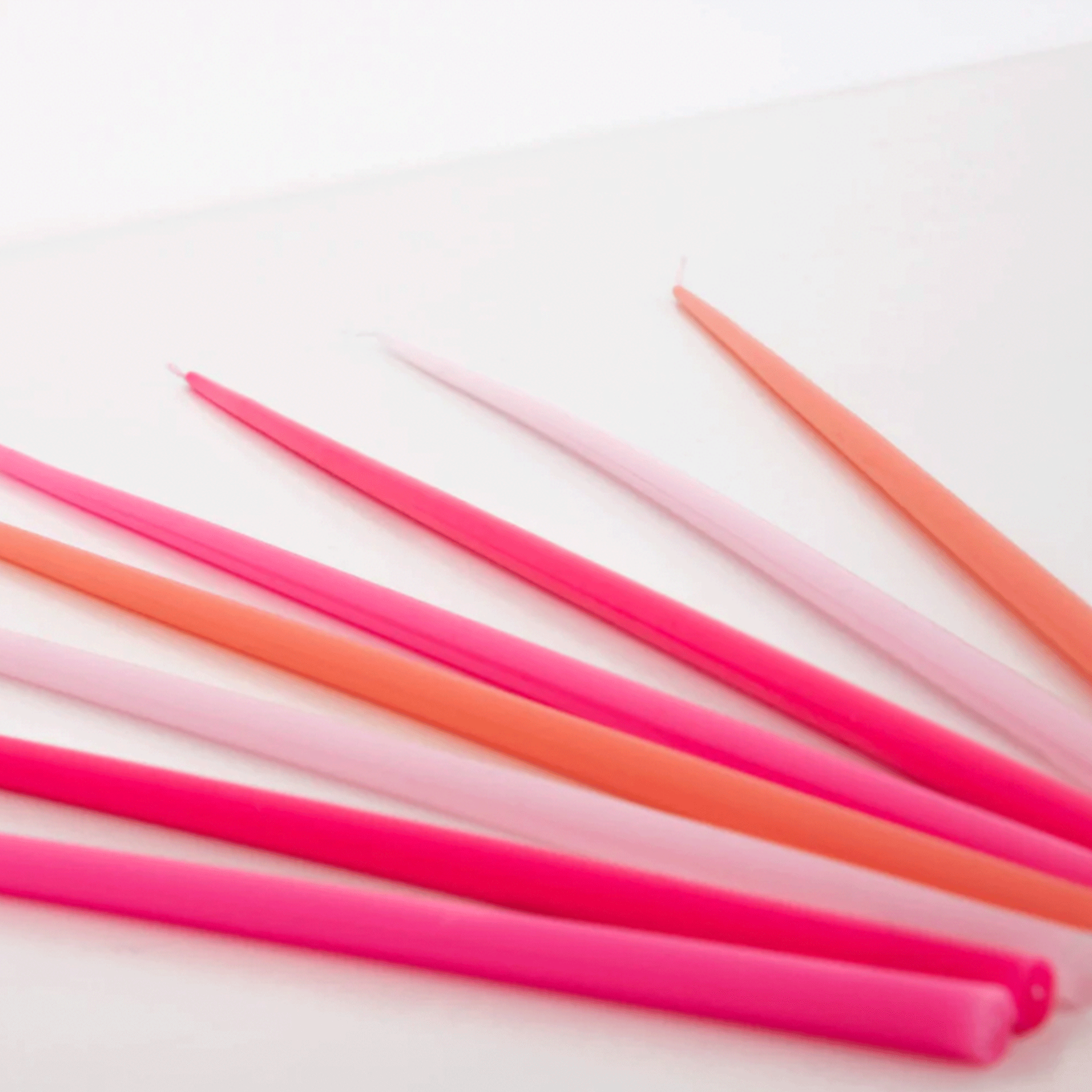 On a white background is a pack of different colored tapered candles in various shades of pink. 