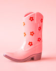 On a pink background is a pink cowboy boot shaped vase with a red and white daisy print on it.