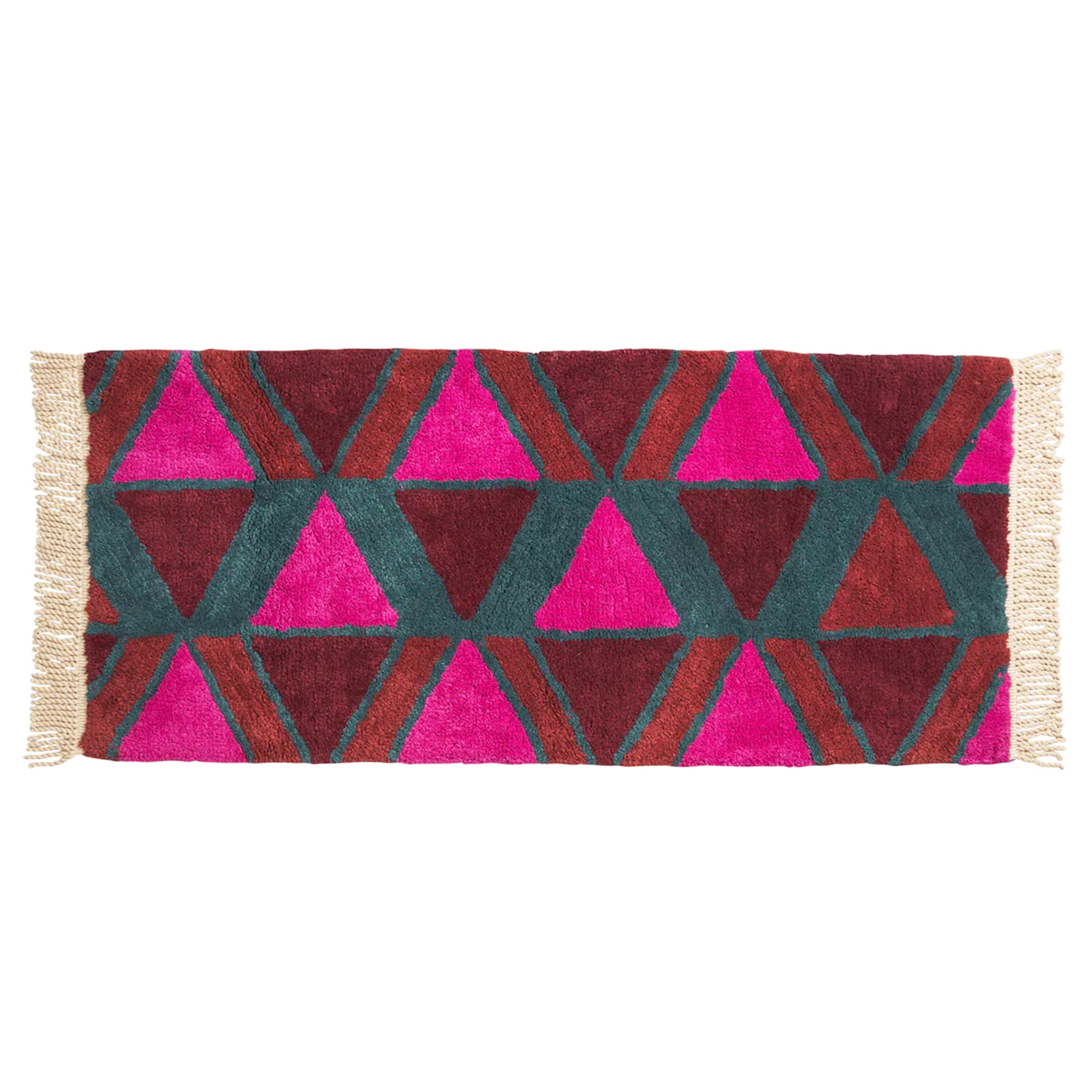 A pink, red, rust and teal triangle patterned bath mat with tassel details on the two ends.