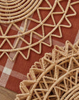 On a rust colored background is a wicker sun shaped placemat.