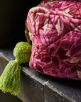 A pink floral patterned cosmetic bag with a green tassel zipper.