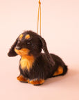 On a green background is a furry black and tan dachshund shaped ornament.