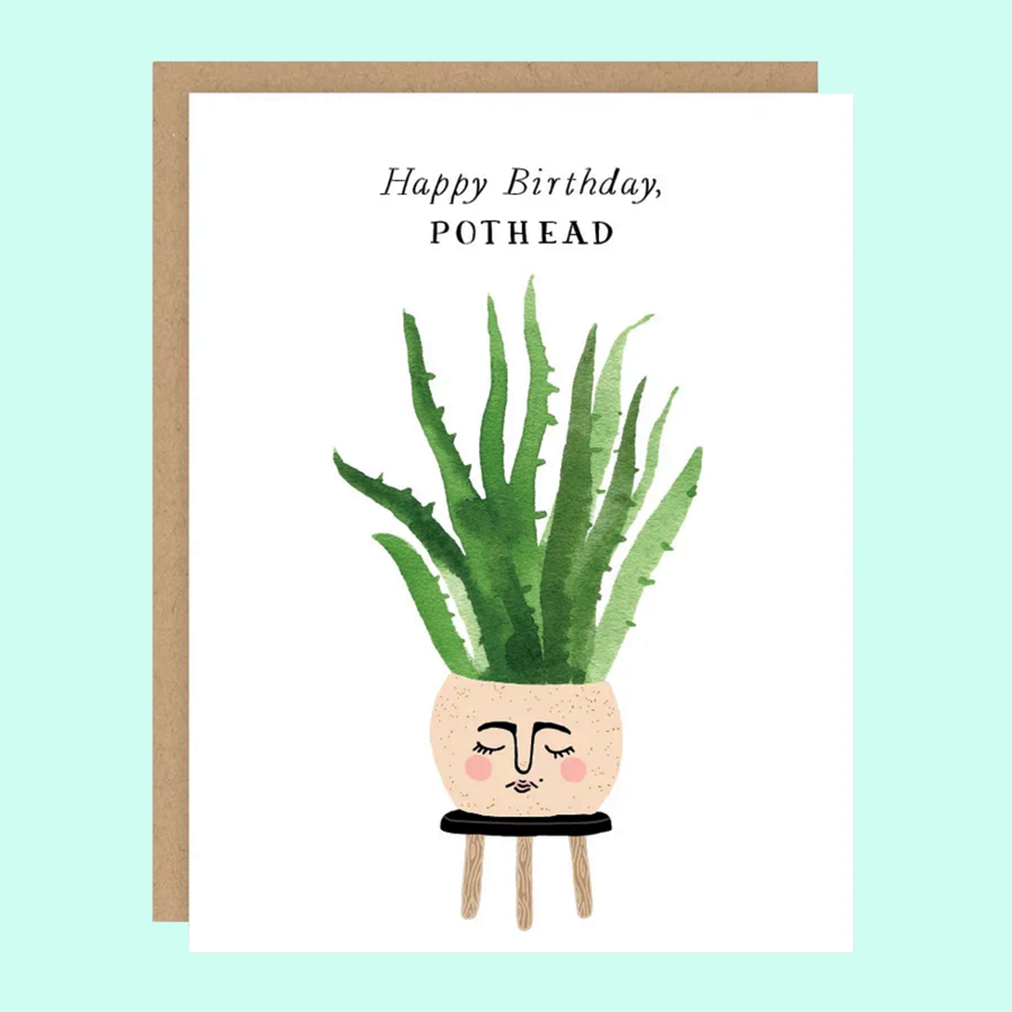 On top of a kraft envelope is a white card. In the middle of the card is a water color painting of a round tan pot sitting on top of a black stool. There is face painted on the front of the pot. Inside the pot is a tall green plant. At the top is black text that reads ‘happy birthday pothead.