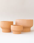 Three different sized tan / light orange ceramic pedestal planters with a ribbed texture.