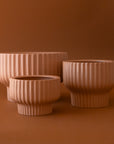 Three different sized tan / light orange ceramic pedestal planters with a ribbed texture.
