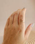 On a tan background is a model's hand with a dainty gold rainbow shaped ring.
