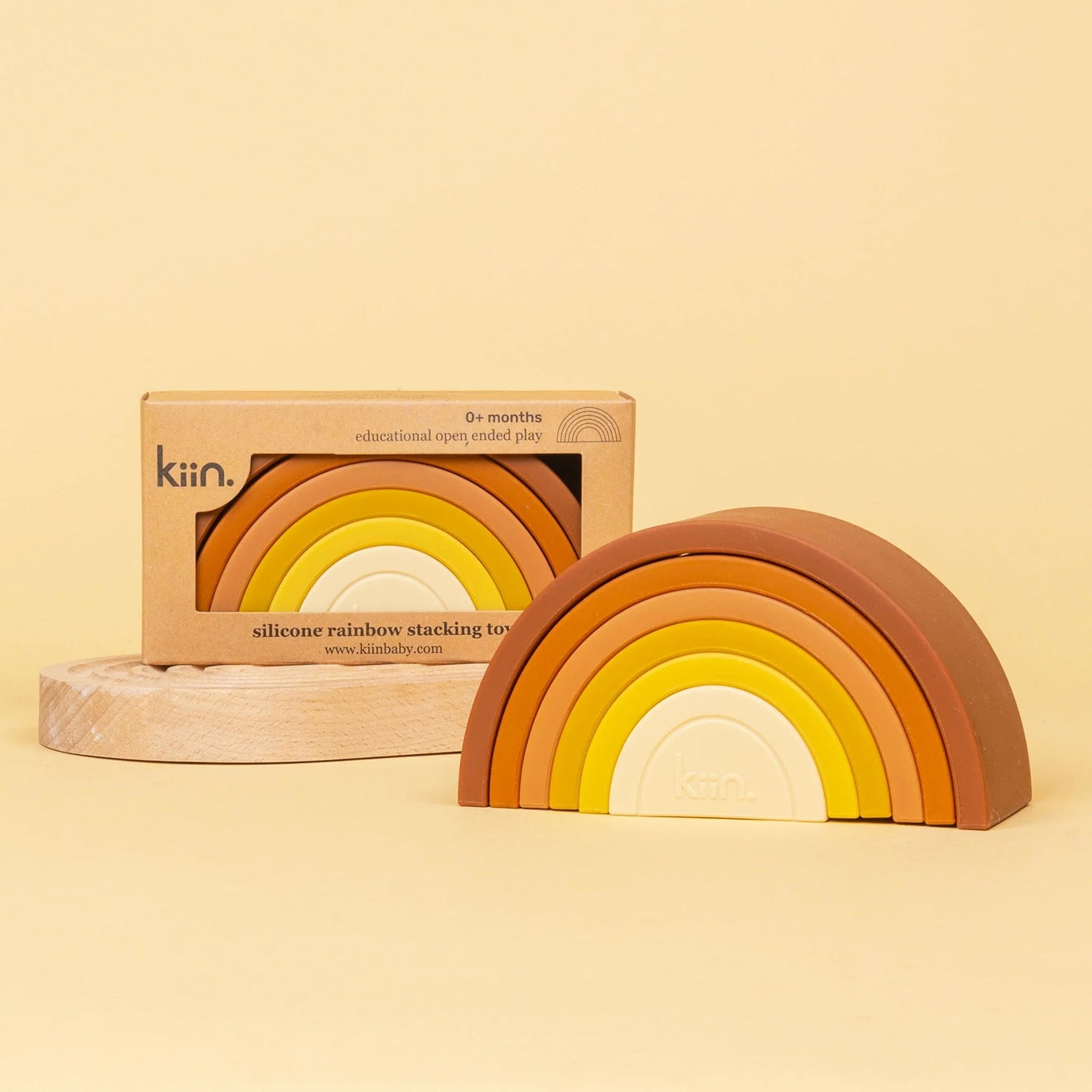 On a yellow background is a silicone stacking toy in the shape of a yellow and orange colored rainbow. 