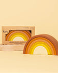 On a yellow background is a silicone stacking toy in the shape of a yellow and orange colored rainbow.