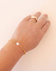 A gold bracelet with a freshwater pearl in the center.