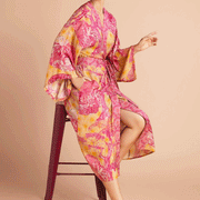On a tan background is a model wearing a pink and yellow/orange robe with a tropical and floral print.