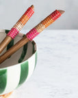 A pair of wooden salad servers with long handles wrapped in orange, pink and neutral