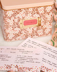 A metal recipe box with a pink daisy pattern with recipe cards and dividers.