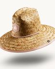 On a white background is a straw hat with a neutral mauve / tan brim underneath and neck strap.