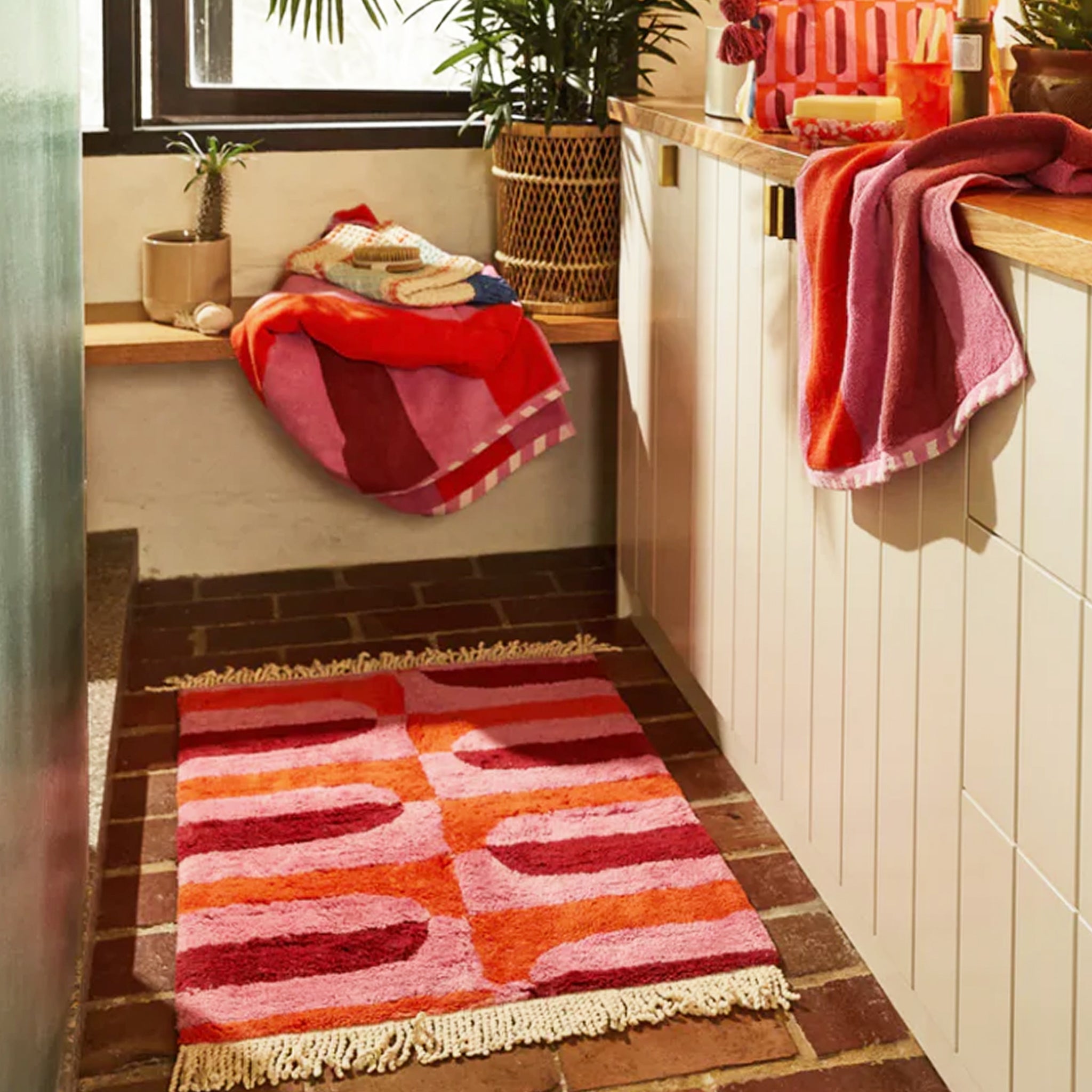 A pink, orange and red bath mat with a tassel detail on each end. 