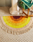 An arch sun shaped yellow, orange and burnt orange bath mat with a tassel edge.