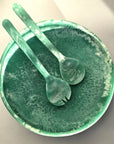 A green resin shallow serving bowl with a set of salad servers.