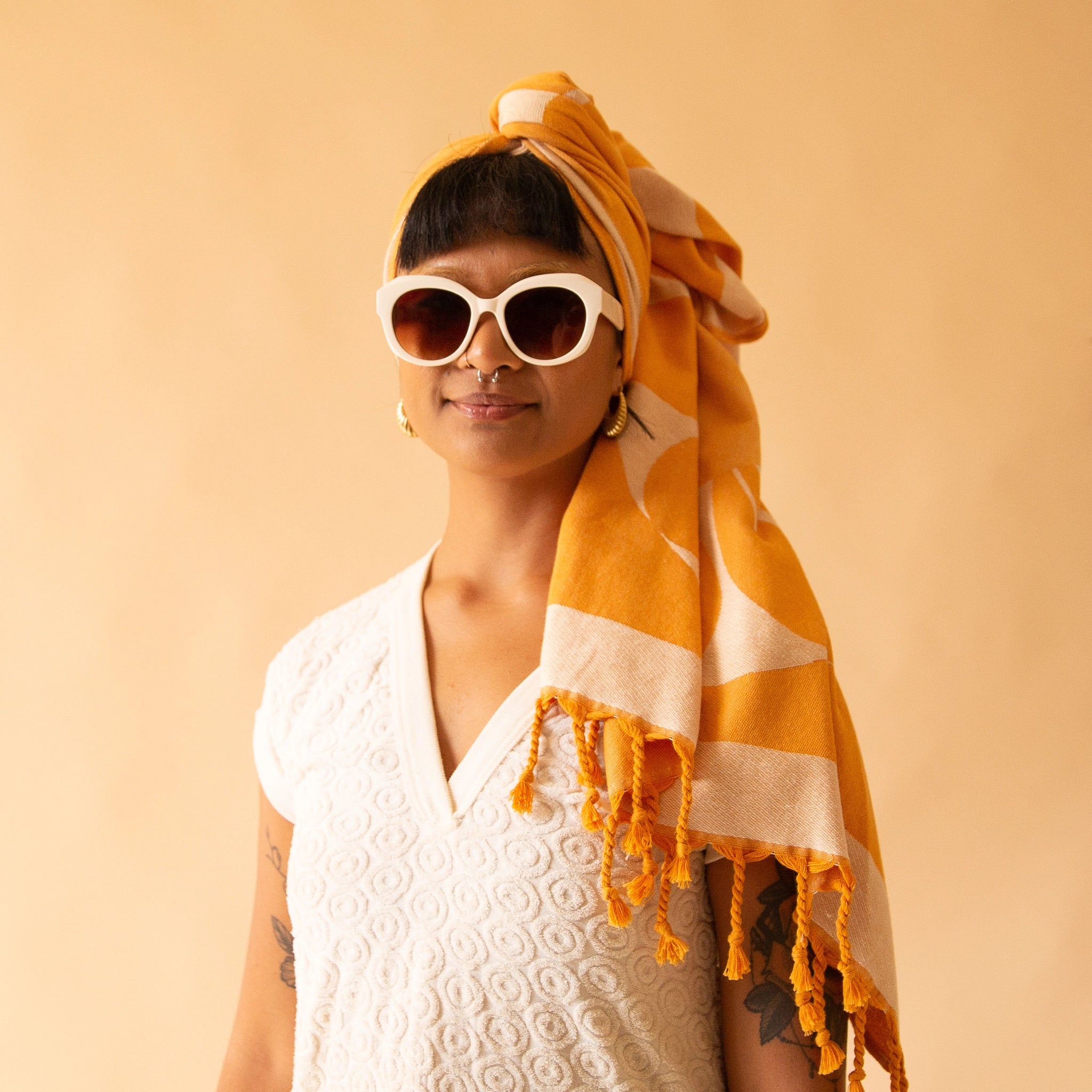 A model in front of a light orange background wearing the Retro Flower Beach Towel around their head.