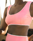A model wearing a 1960's inspired swim suit with a wavy edge detail and high waist bottoms. The color of the swim suit is a coral pink hue.