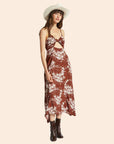 On a tan background is a rust colored dress with an ivory tropical print and a tie detail.