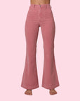 On a pink background is a model wearing the pink corduroy pants with front pockets and a flare bottom.
