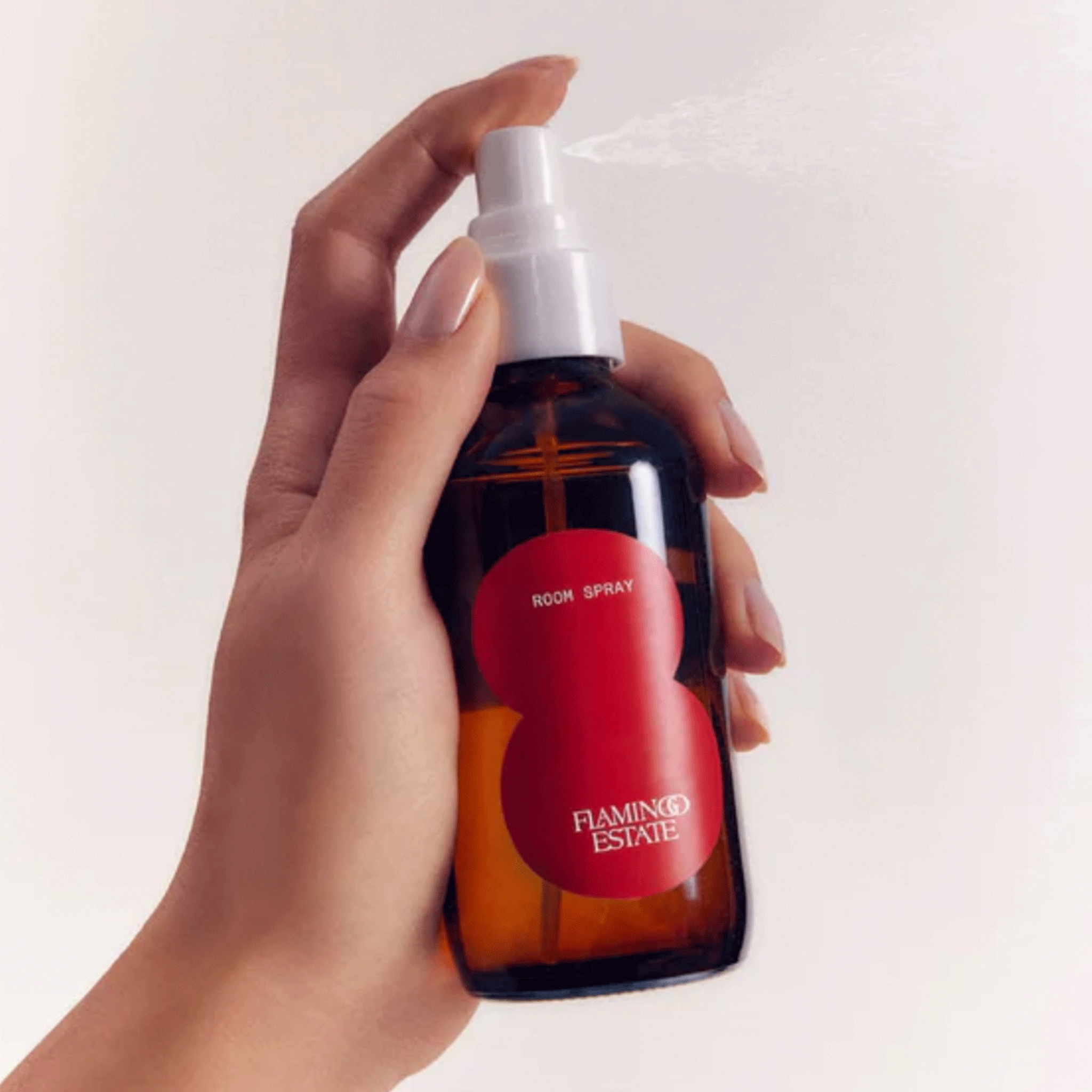 On a white background is a glass spray bottle with a red circle logo on the front that reads, &quot;Room Spray Flamingo Estate&quot;. 