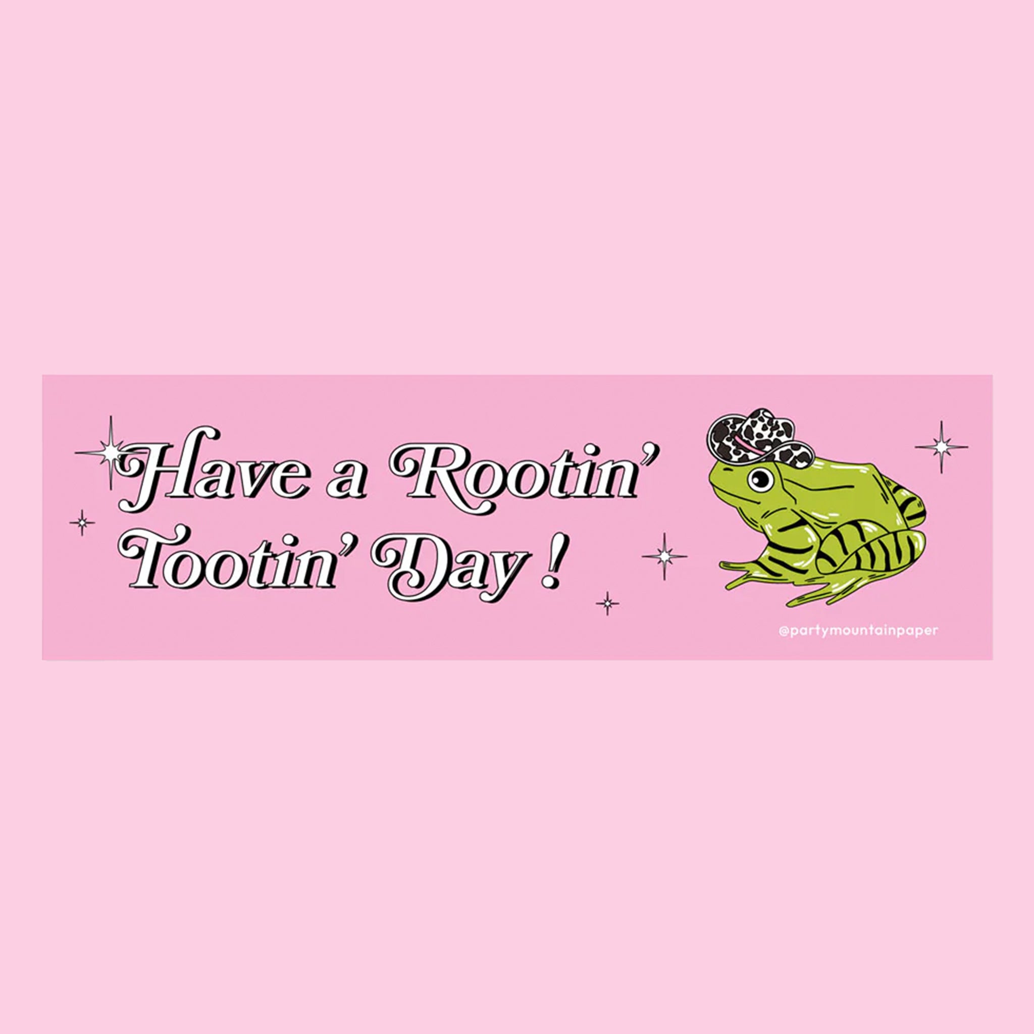 On a pink background is a pink bumper sticker with an illustration of a green frog with a cow print cowboy hat on and text that reads, "Have a Rootin' Tootin' Day!". 