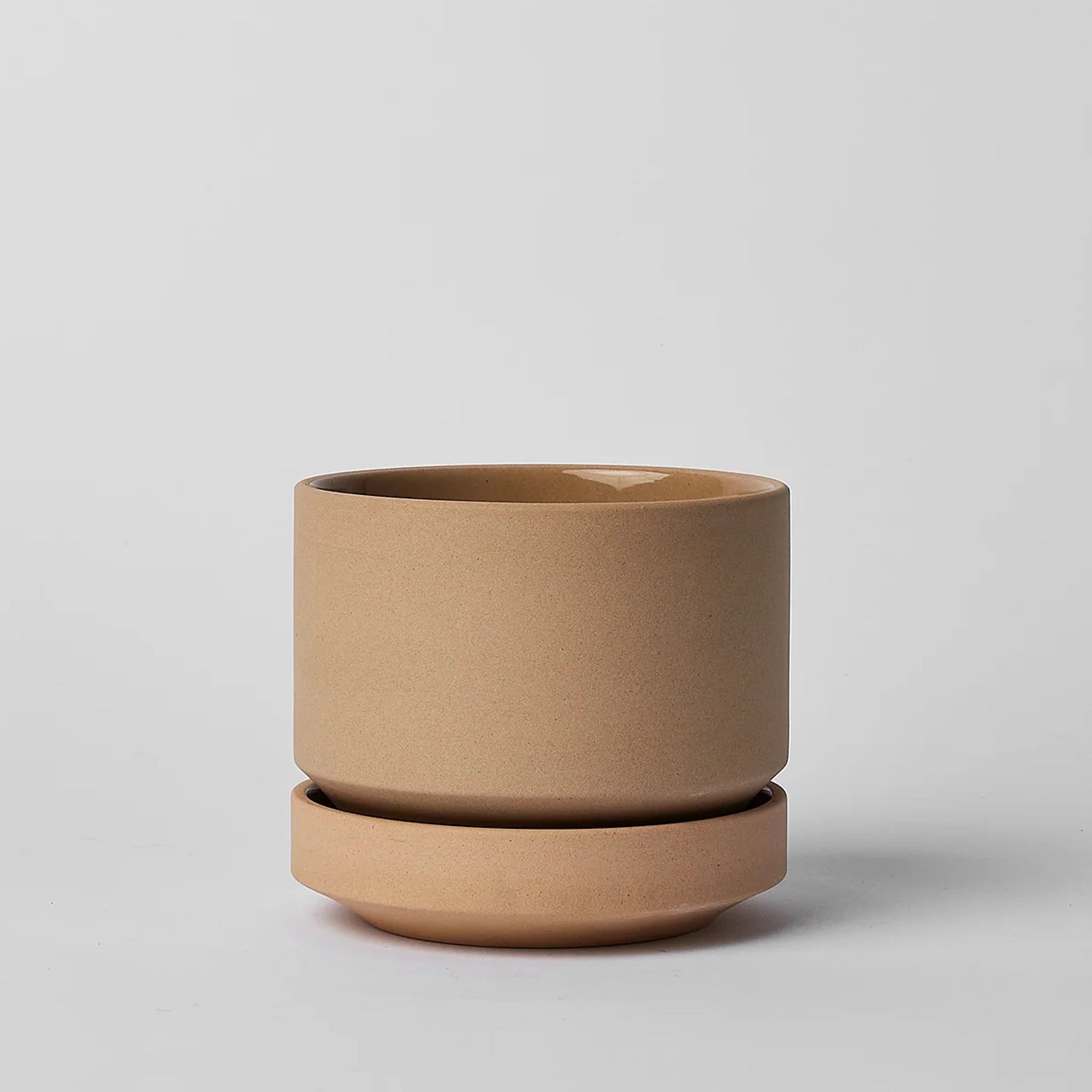 On a neutral background is a tan ceramic planter with a thick removable tray for watering. 