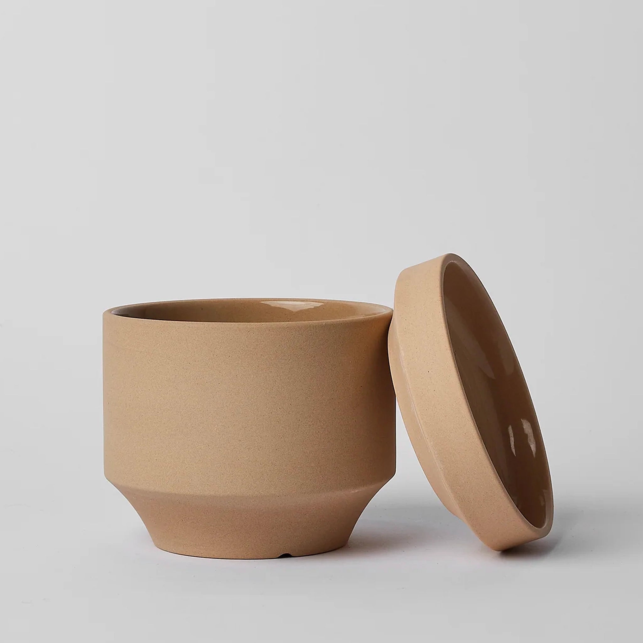 On a neutral background is a tan ceramic planter with a thick removable tray for watering