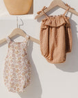 A children's romper with a light pink and yellow floral pattern next to the ruffle romper in the shade grapefruit.